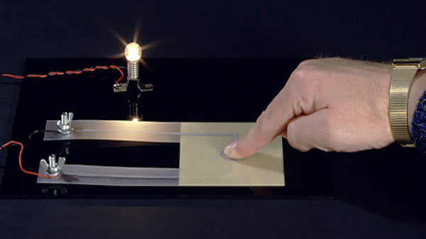 Finger tippt auf Folie und bringt Glühbirne zum leuchten